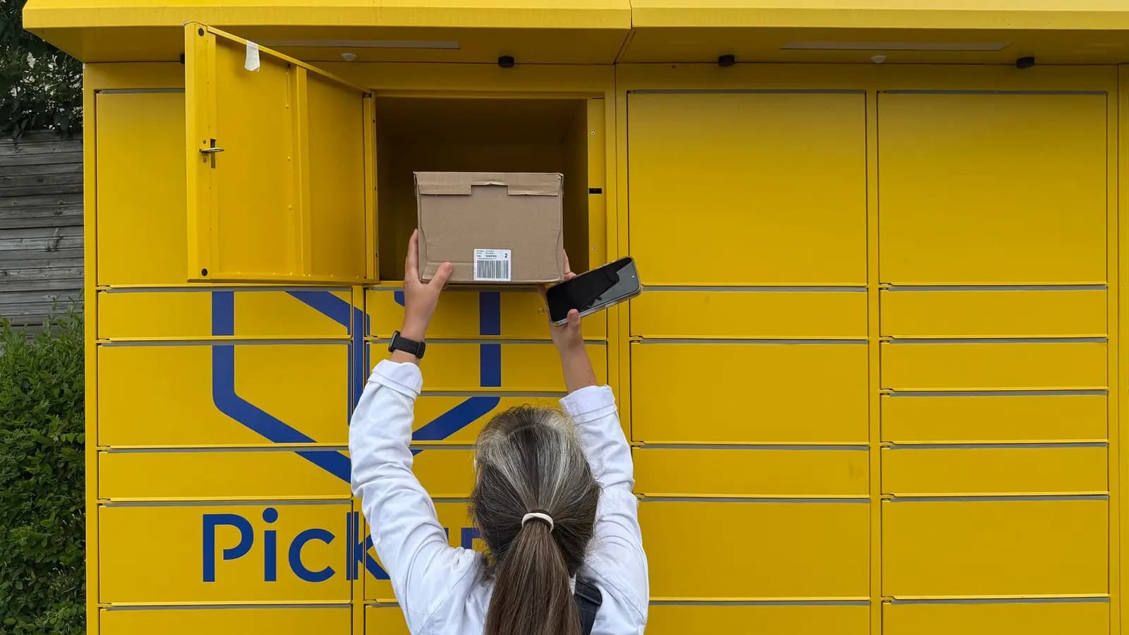 Person holt ein Paket aus einer gelben Paketstation