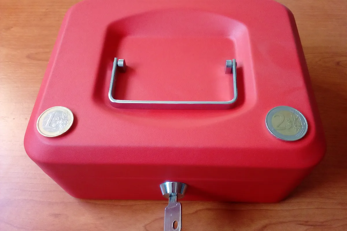 Rote Geldkassette mit zwei Euromünzen auf einem Holztisch