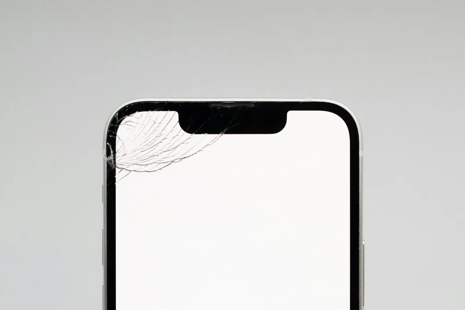 Oberer Teil eines iPhone von vorn mit weißem Display und einem Glasriss in der linken oberen Ecke