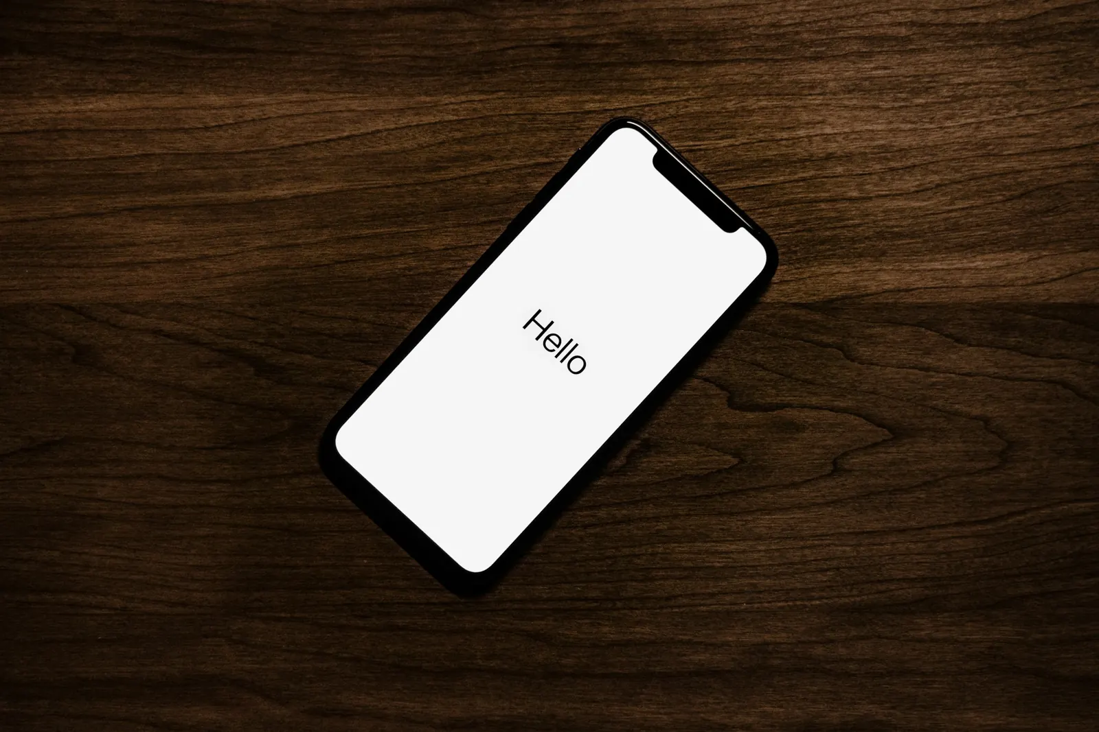 iPhone auf einem Holztisch, auf dem Display der Begrüßungsbildschirm der Einrichtung mit dem Wort „Hello“