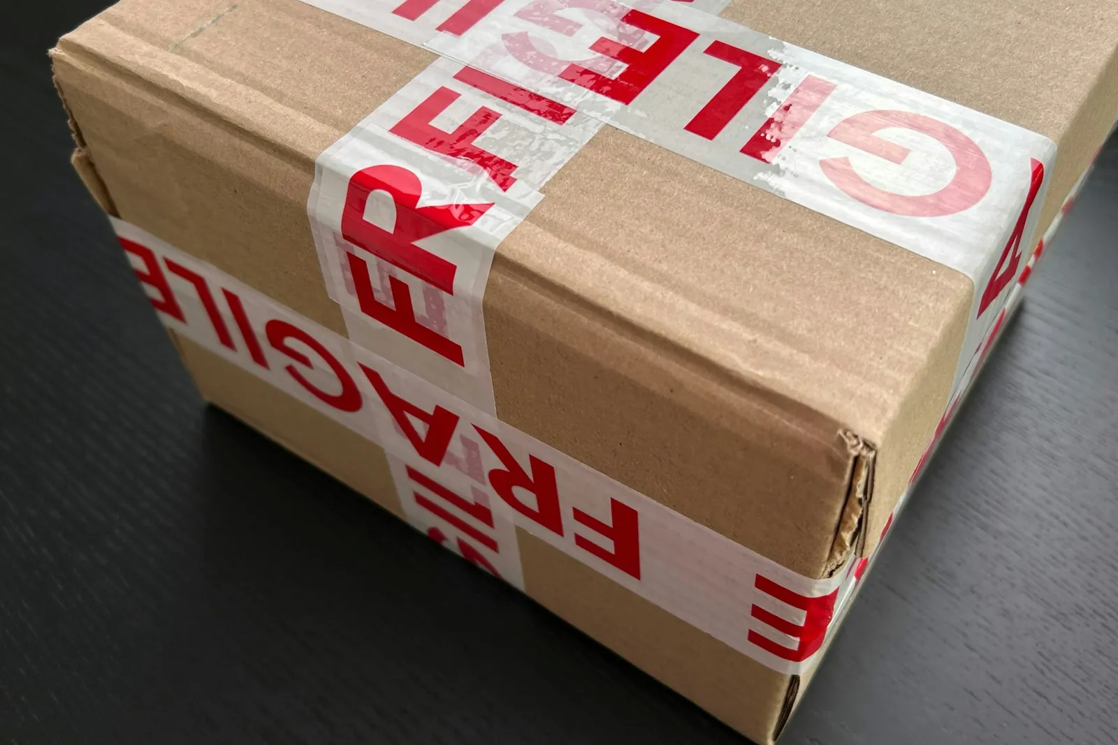 Brauner Versandkarton, rundum mit rotem Klebeband mit der Aufschrift „Fragile“ verklebt