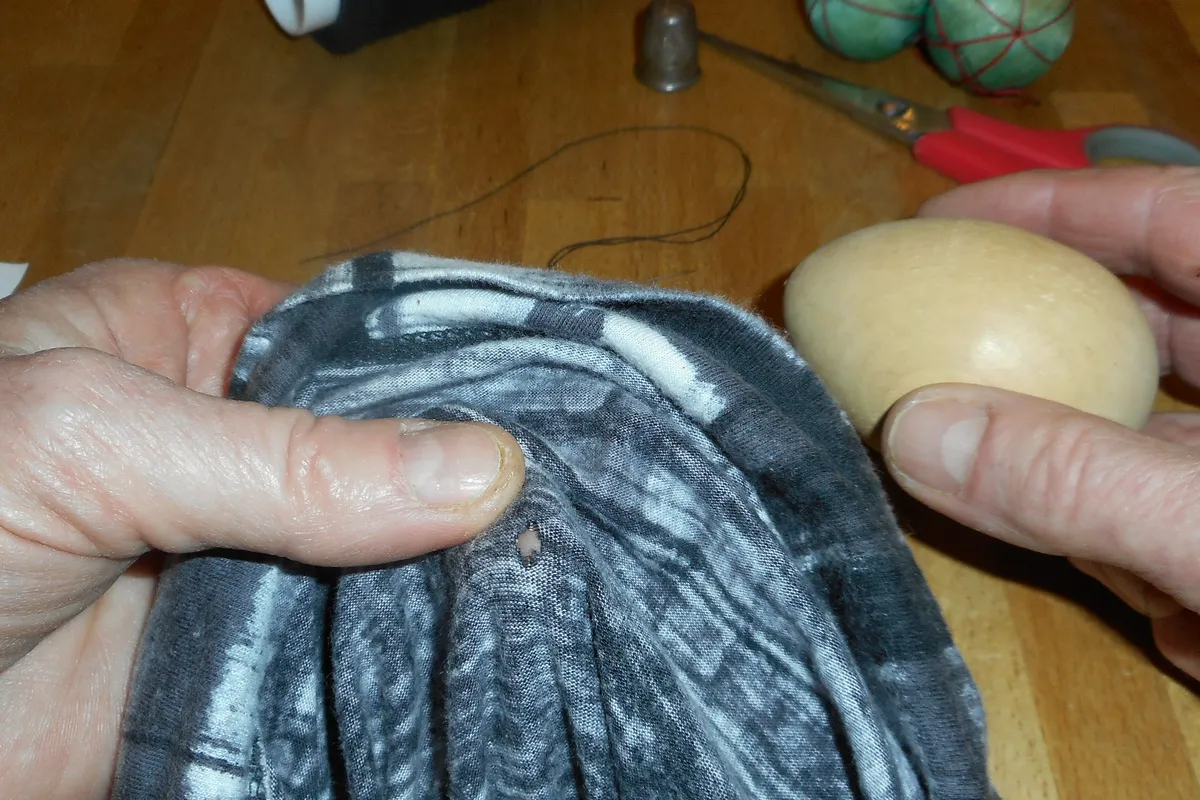 Hände halten einen grauen Wollpullover mit einer dünnen Stelle über einen Stopfpilz