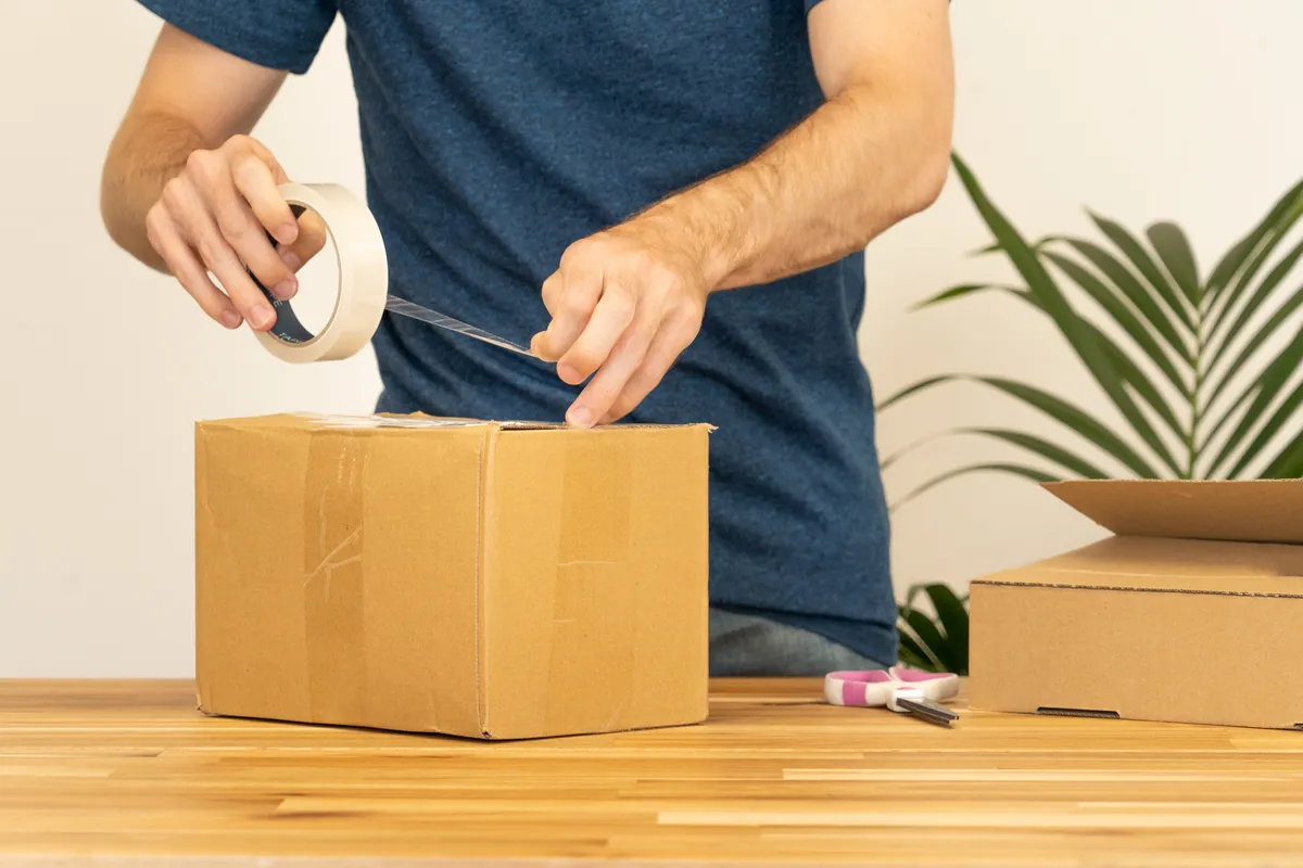 Eine Person verschließt einen Versandkarton mit Klebeband